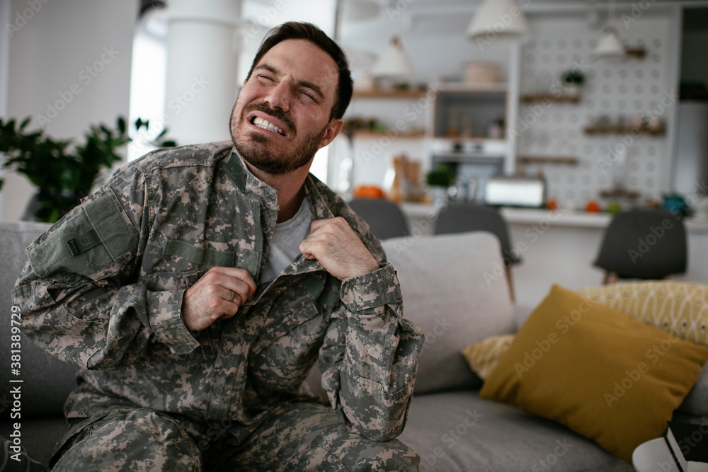 Fototapeta premium Depressed soldier sitting on sofa in living room. Young marine having PTSD..
