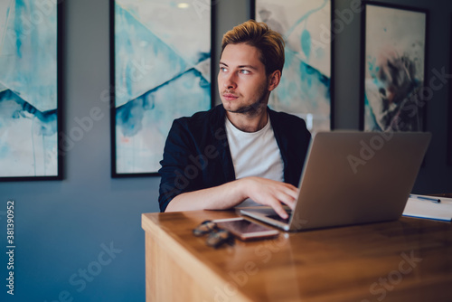 Young man using laptop and looking away in office