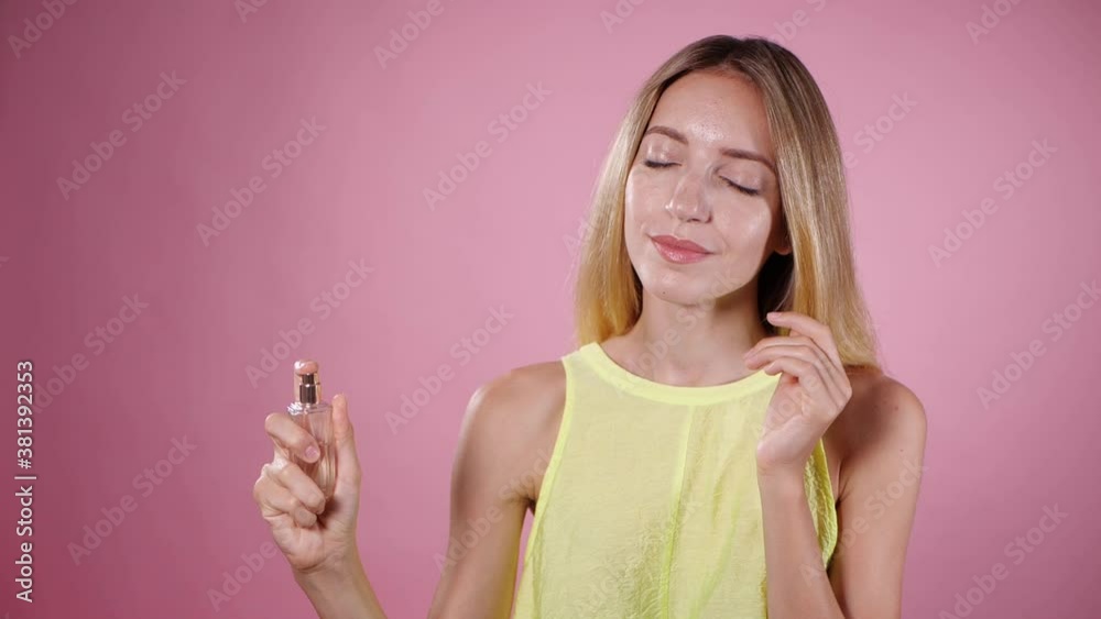 Beautiful woman spraying on perfume against pink background. Slow motion Beautiful woman spraying on perfume against pink background. Slow motion