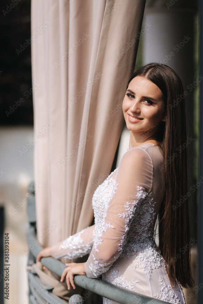Fototapeta premium Beautiful young model in evening drees posing to photographer by the big window