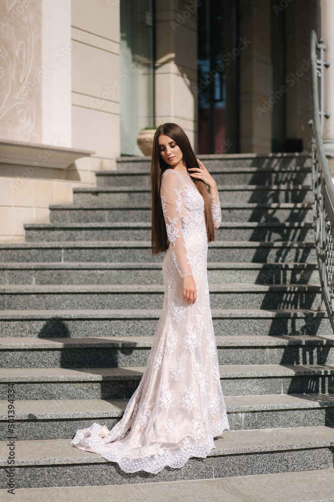 Fototapeta premium Gorgeous model in wedding dress stand on stair by big restaurant