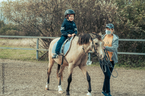 A child with special needs is riding with a close supervision teacher. This is a treatment called Hippotherapy, Life in the education age of disabled children, Happy disability kid concept. quarantine © Air_Lady