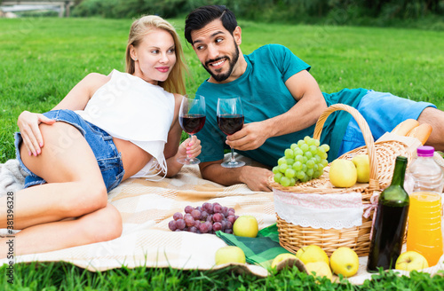 Satisfied couple are talking and drinking wine in time picnic outdoor