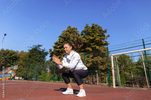 Focused black-haired girl in white hoodie and black pants trains alone in red stadium