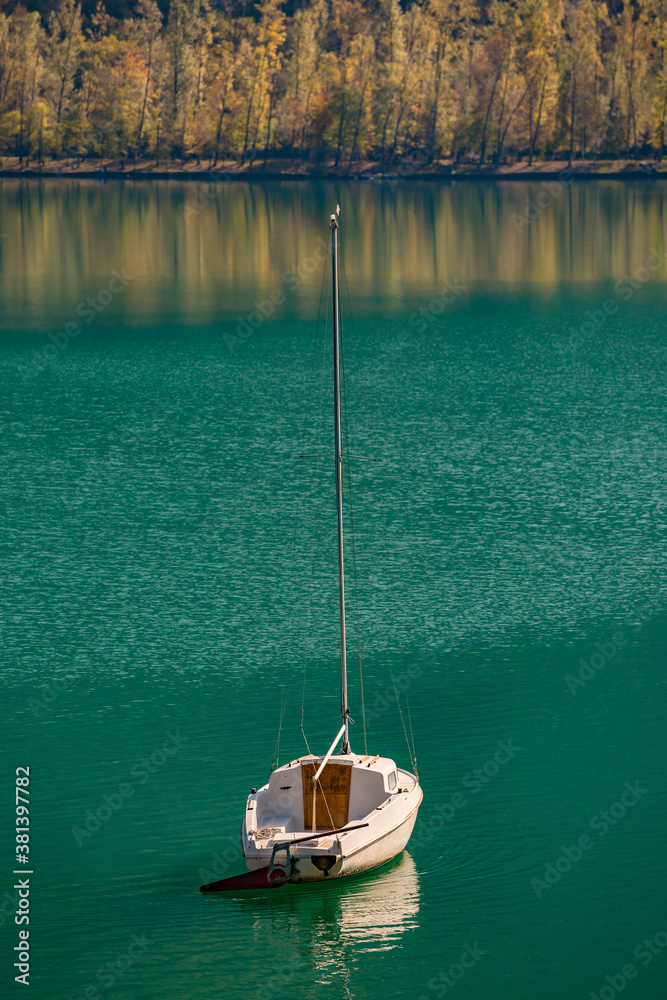 Beautiful autumn view of Cavazzo lake in Friuli Venezia Giulia, Italy. Small white boat on crystal clear emerald lake waters Beautiful autumn view of Cavazzo lake in Friuli Venezia Giulia, Italy. Small white boat on crystal clear emerald lake waters