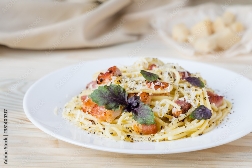 Pasta Carbonara. Spaghetti with bacon, parmesan cheese and basil on white plate on light wooden background. Italian food concept. Selective focus. Pasta Carbonara. Spaghetti with bacon, parmesan cheese and basil on white plate on light wooden background. Italian food concept. Selective focus.