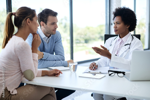 African American female doctor having consultations with a couple at medical clinic.