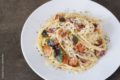 Pasta Carbonara. Spaghetti with bacon, parmesan cheese and basil on white plate on wooden background. Italian food concept. Top view, close-up.