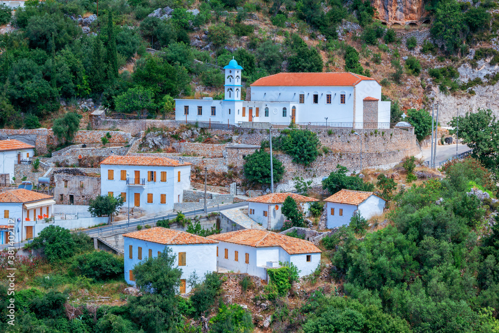 View of Albanian village - traditional white houses with orange roofs and wooden shutters on windows - on the mountain hill, small church and road.