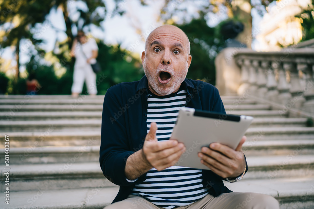 Amazed senior man using tablet on stairs in park