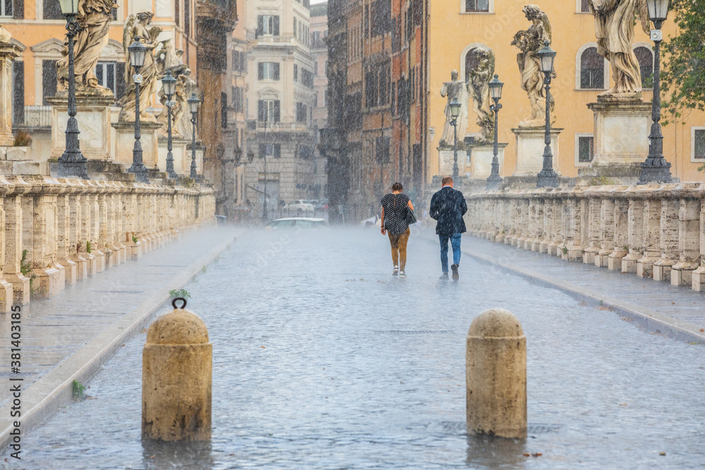 Rain in the historic center of Rome in Italy. Two people back to back walking under the storm. Sant Angelo bridge.
