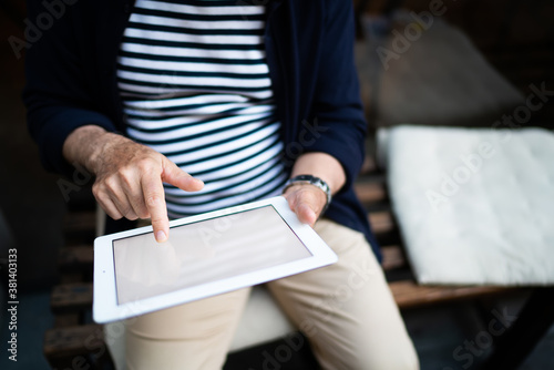 Faceless senior man browsing tablet on bench in street
