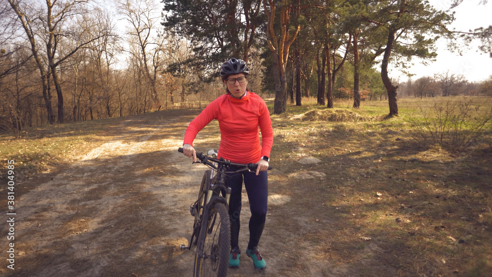 Fototapeta premium The topic health problems with athletes. Caucasian woman cyclist on mountain bike finish workout in forest. Emotion tired, hard fast heart beating and hard to breathe. Cardiac pathology tachycardia