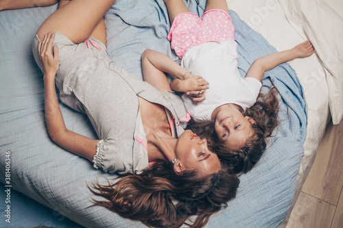 Happy loving family lying relaxing and enjoying in bedroom together. Mother and her cute preschool daughter child girl in pajamas playing and hugging in bed in the morning top view. Happy mother's day