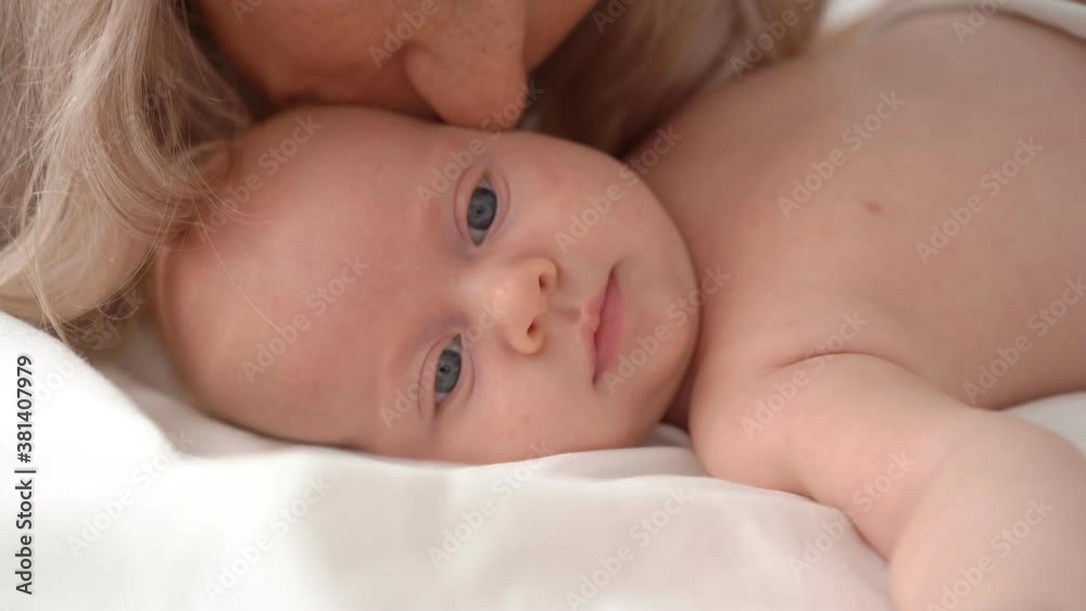 mom kisses the baby lying in bed. concept of maternal love, newborn care. mom kisses the baby lying in bed. concept of maternal love, newborn care.