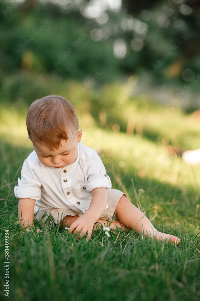 Happy adorable baby boy sitting on the grass in the park on summer day. Child in trendy and cute clothes Happy adorable baby boy sitting on the grass in the park on summer day. Child in trendy and cute clothes