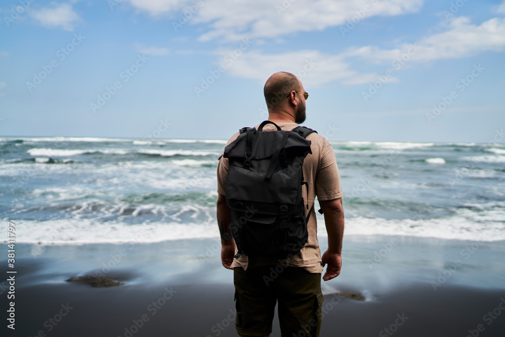 Unrecognizable man with backpack standing on seashore