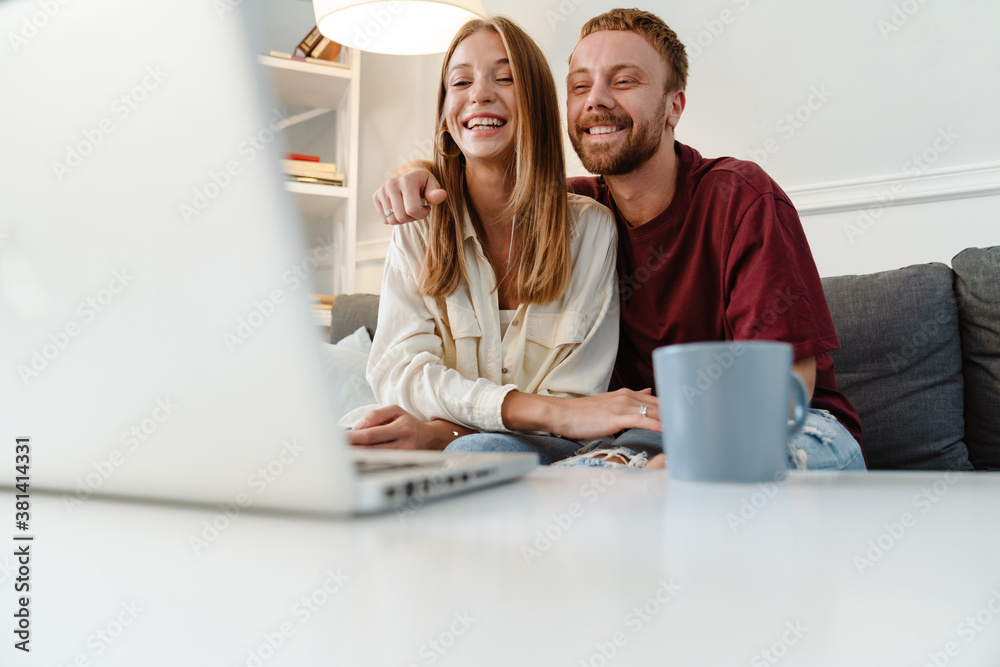 Image of ginger couple laughing and using laptop while sitting on sofa Image of ginger couple laughing and using laptop while sitting on sofa