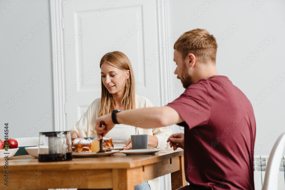Image of joyful couple drinking coffee with pie while sitting at table Image of joyful couple drinking coffee with pie while sitting at table