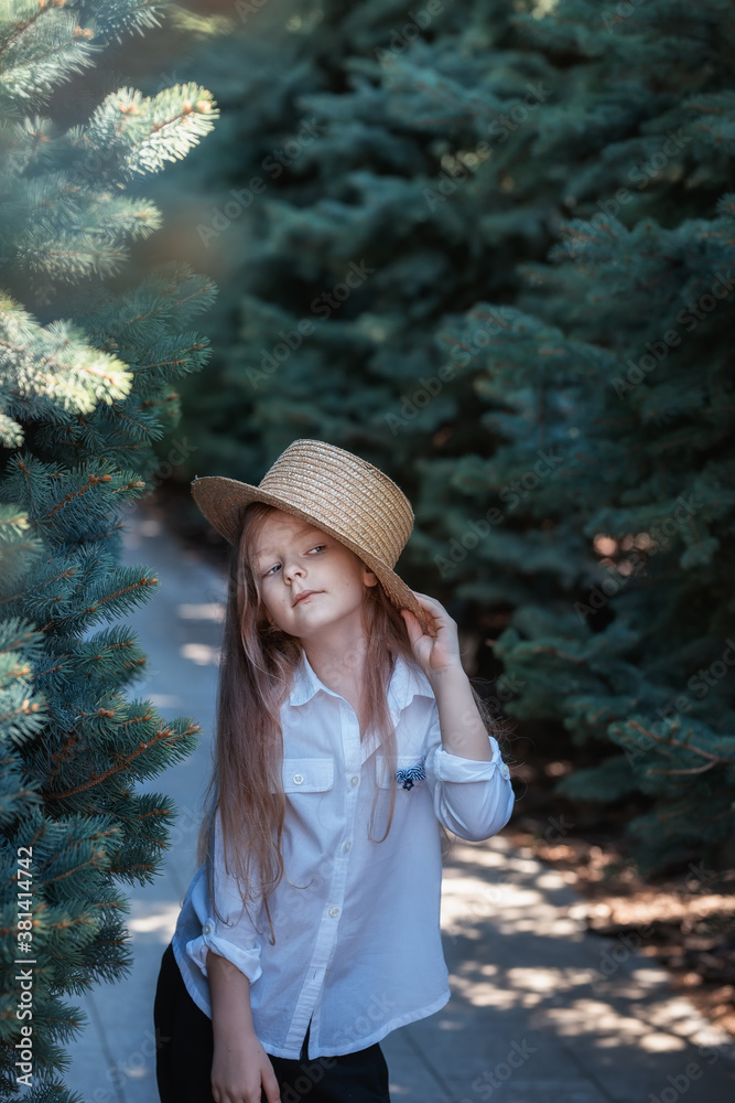 Girl in a straw hat posing among green fir trees