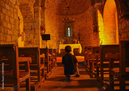 ROCABRUNA, CATALONIA, SPAIN, EUROPE, SEPTEMBER 2020. Interior of the 12th century Romanesque church in the medieval city of Rocabruna. Kneeling in front of the altar is a boy on his back.