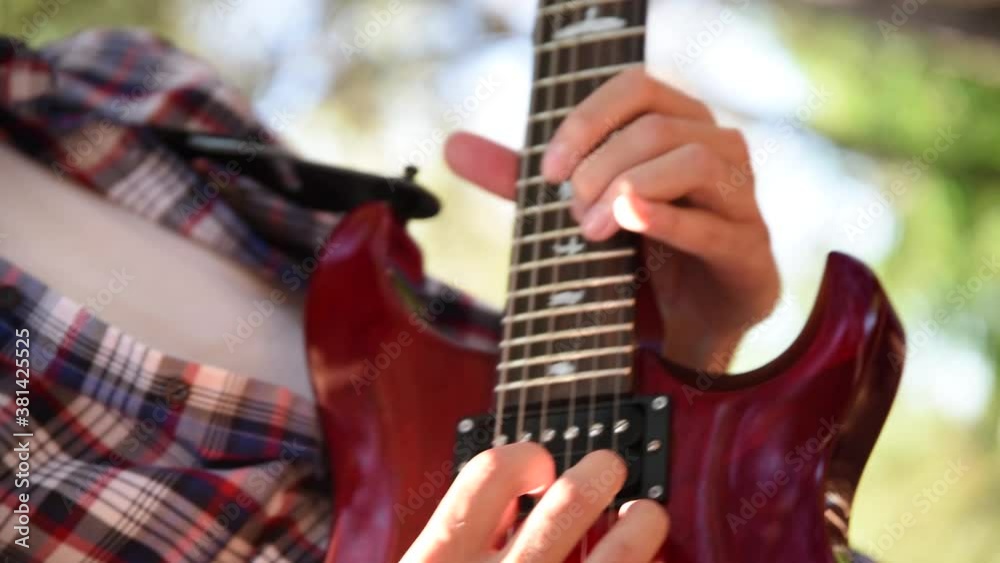 Artist playing electric guitar in a red plaid shirt. Rock musician playing electric guitar