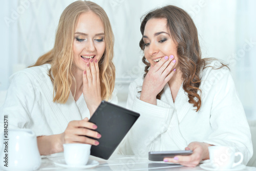 Young women in bathrobes using digital devices