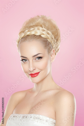 Frontal portrait of a cute blonde young woman with bright make-up and hairstyle, with bare schoulders, over pink background.