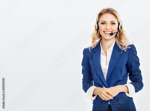 Call center. Smiling female support phone operator in blue confident suit and headset, isolated over grey background. Caucasian blond model in customer service help consulting concept.