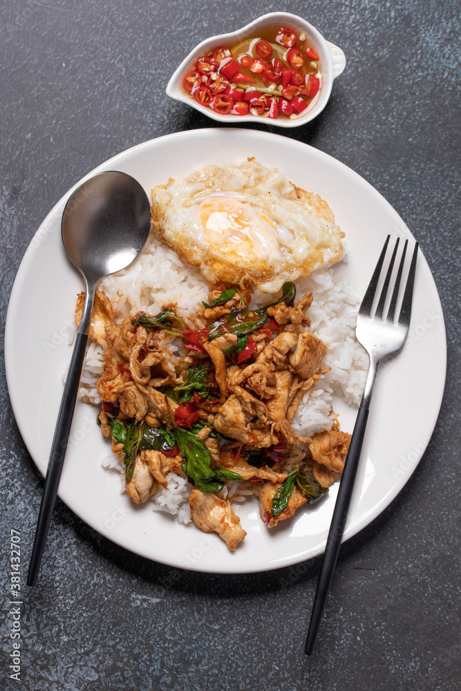 Chicken basil rice with fried egg in white plate on black background. Popular Thai food. Chicken basil rice with fried egg in white plate on black background. Popular Thai food.