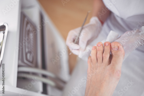 Professional medical pedicure procedure close up using double nail instrument. Patient visiting chiropodist podiatrist. Foot treatment in SPA salon. Podiatry clinic. Pedicurist hands in white gloves.