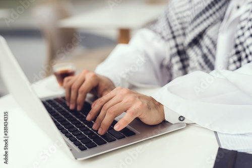 Young Arabian Man in Scarf Using Laptop in Cafe.