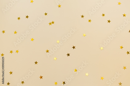 Golden confetti on beige paper trendy background. Festive holiday backdrop. Birthday congratulations, Christmas , Valentines day, New Year. Flat lay, top view, copy space.