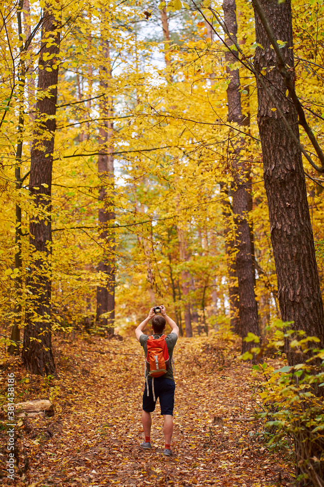 Young man-photographer walking in the golden autumn forest and making photos.