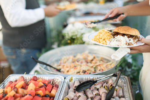 Картината върху платно Close up of bridal party dishing up catered buffet food at casual outdoor weddin