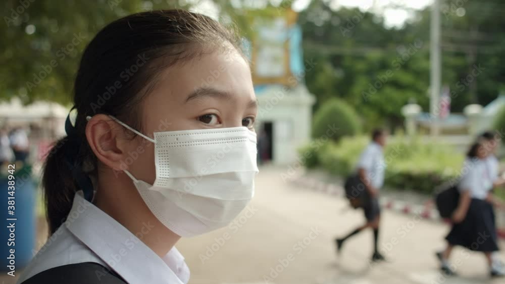 An Asian female students in white high school uniforms wearing the masks stand on the side of the road waiting for cars to go back home after school during the Coronavirus 2019 (Covid-19) epidemic. An Asian female students in white high school uniforms wearing the masks stand on the side of the road waiting for cars to go back home after school during the Coronavirus 2019 (Covid-19) epidemic.