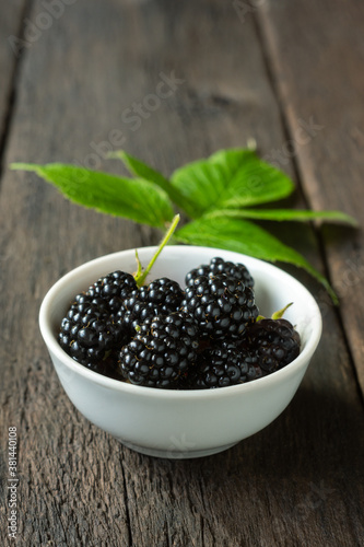A bowl of ripe blackberries on a wooden table. Cultivated berries, harvest season