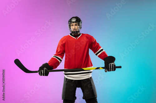 Confidence. Male hockey player with the stick on ice court and neon gradient background. Sportsman wearing equipment, helmet practicing. Concept of sport, healthy lifestyle, motion, wellness, action. © master1305
