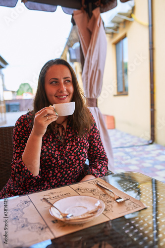 Girl sits at a table in a cafe and drinks waugh smiles photo