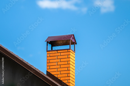 Red brick ventilation chimney on the roof of the house against the blue sky.