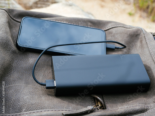 The phone is charged using a power Bank. Use of modern technologies in everyday life. The phone and powerBank are in the tourist's leather backpack. Convenient modern gadgets for a comfortable life