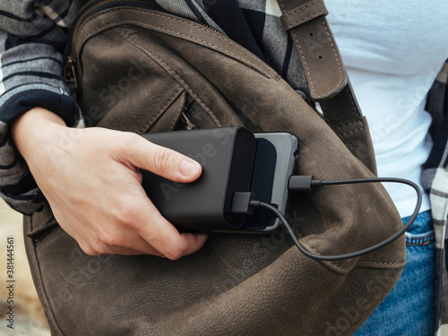 The girl uses a smartphone connected to the power Bank. Black smartphone and powerBank in women's hands close-up. Using gadgets in the modern world. The concept of portable chargers, modern tourism