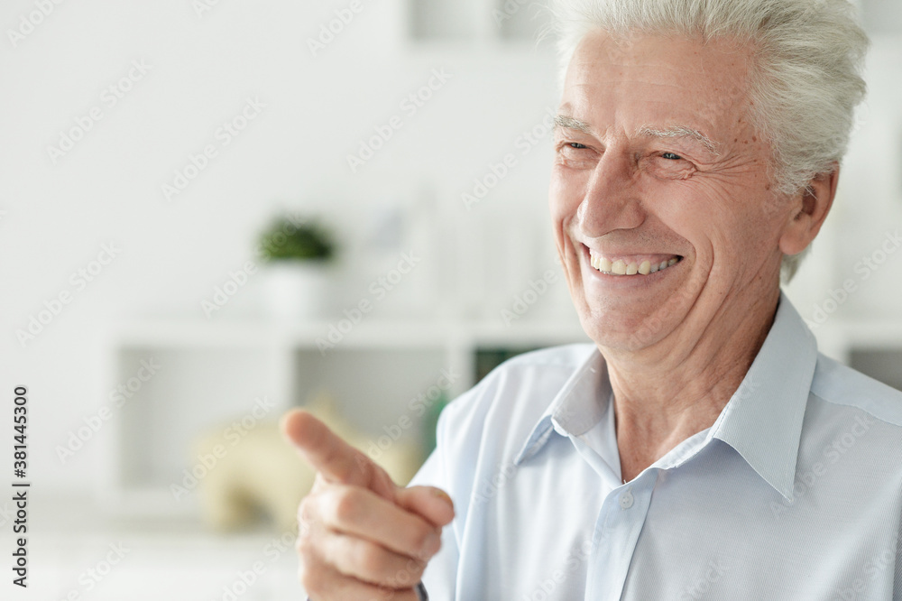 Smiling senior man pointing with finger at home