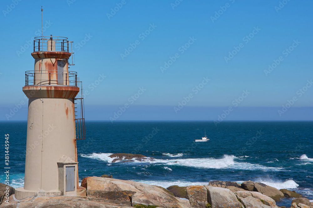 Fishing boat sailing near the Punta de la Barca lighthouse in the fishing village of Muxía, Costa da Morte, Galicia, Spain