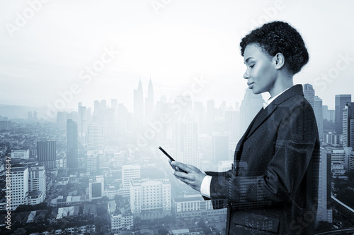 Attractive black African American business woman in suit using smart phone and thinking how to tackle the problem, new career opportunities, MBA. Kuala Lumpur on background. Double exposure.