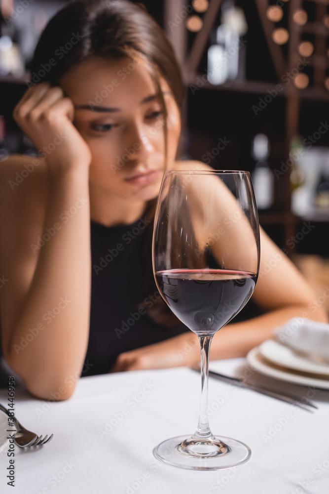 Selective focus of glass of wine near upset woman in restaurant
