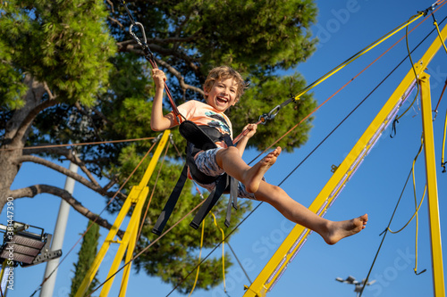 Children have fun jumping on bungee trampoline secured with rubber bands. Sunny day