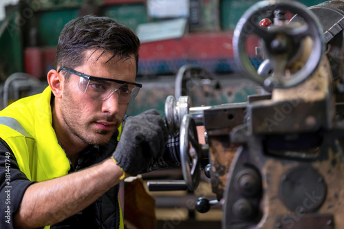 Engineer or supervisor wearing safety glass and glove, concentrate on adjusting the gap of the milling (lathe) machine at the iron manufacturing factory. Heavy sweating on his face. Industrial area..