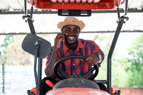 African farmer using smartphone and driving tractor in farm during harvest in countryside. Agriculture or cultivation concept