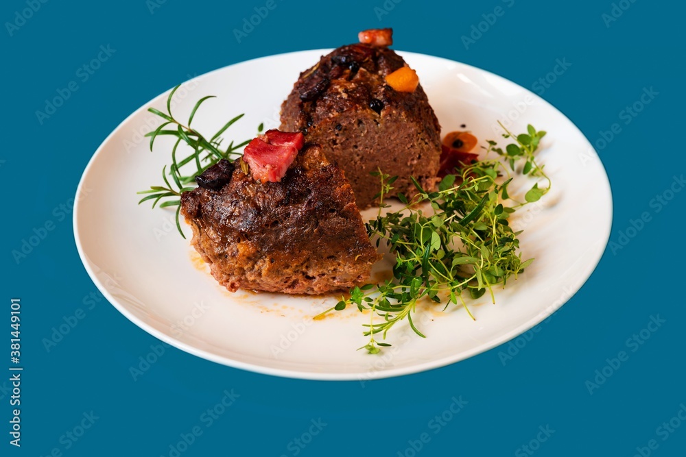 Baked meatloaf with herbs on white plate.